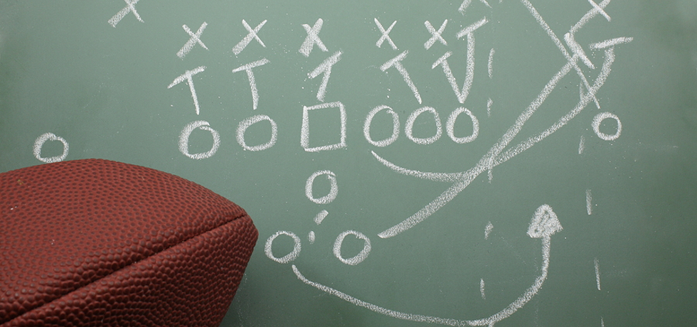 An Xs and Os football play on a chalkboard with a football nearby.