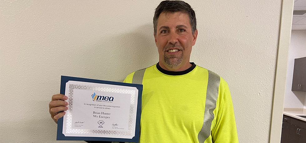 We Energies troubleshooter Brian Hunter holding an award certificate for helping save a man's life.