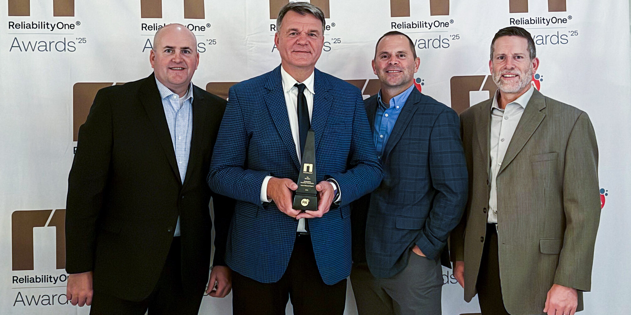 Four men taking a photo with a black and gold trophy from Reliability One
