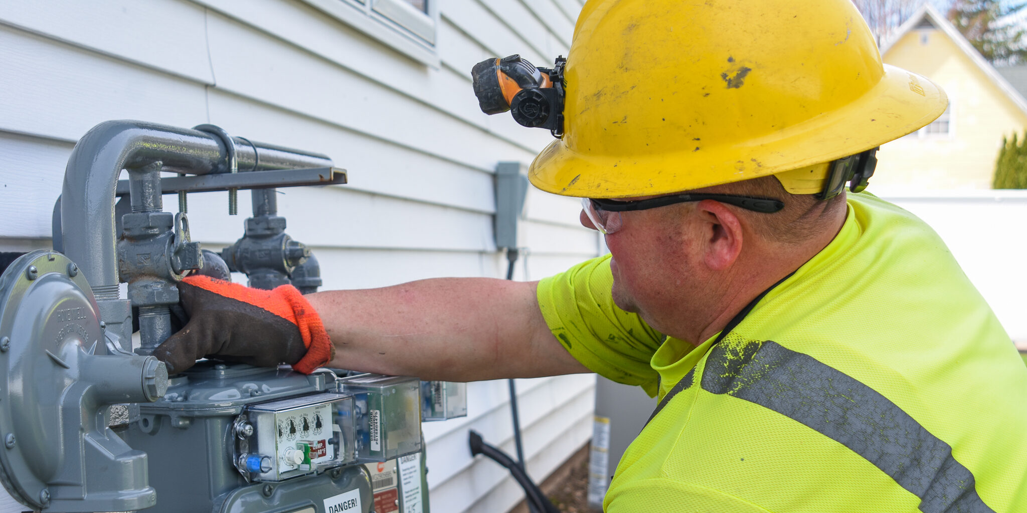 A natural gas utility technician works to repair a meter damaged by floodwater on a sunny day.