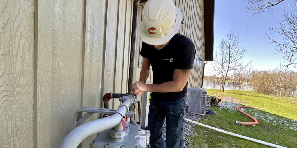 A We Energies natural gas worker works on a natural gas meter near a home on a sunny day.